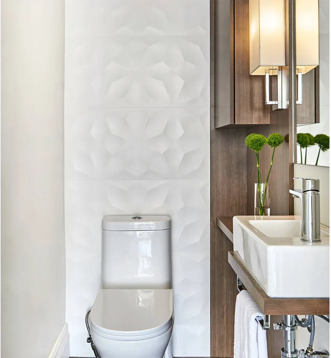 White sculptural tiles behind a toilet beside a wood-backed wall-mounted basin and narrow ledges.