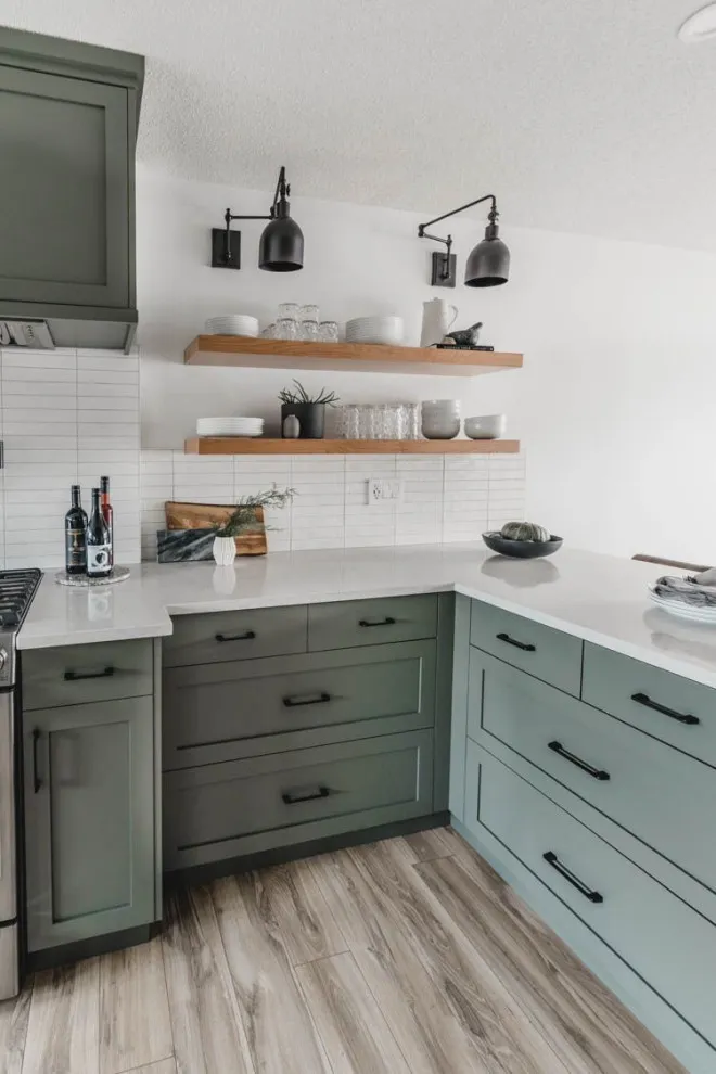 Muted sage lower cabinets sit beneath timber shelves and a pale wall