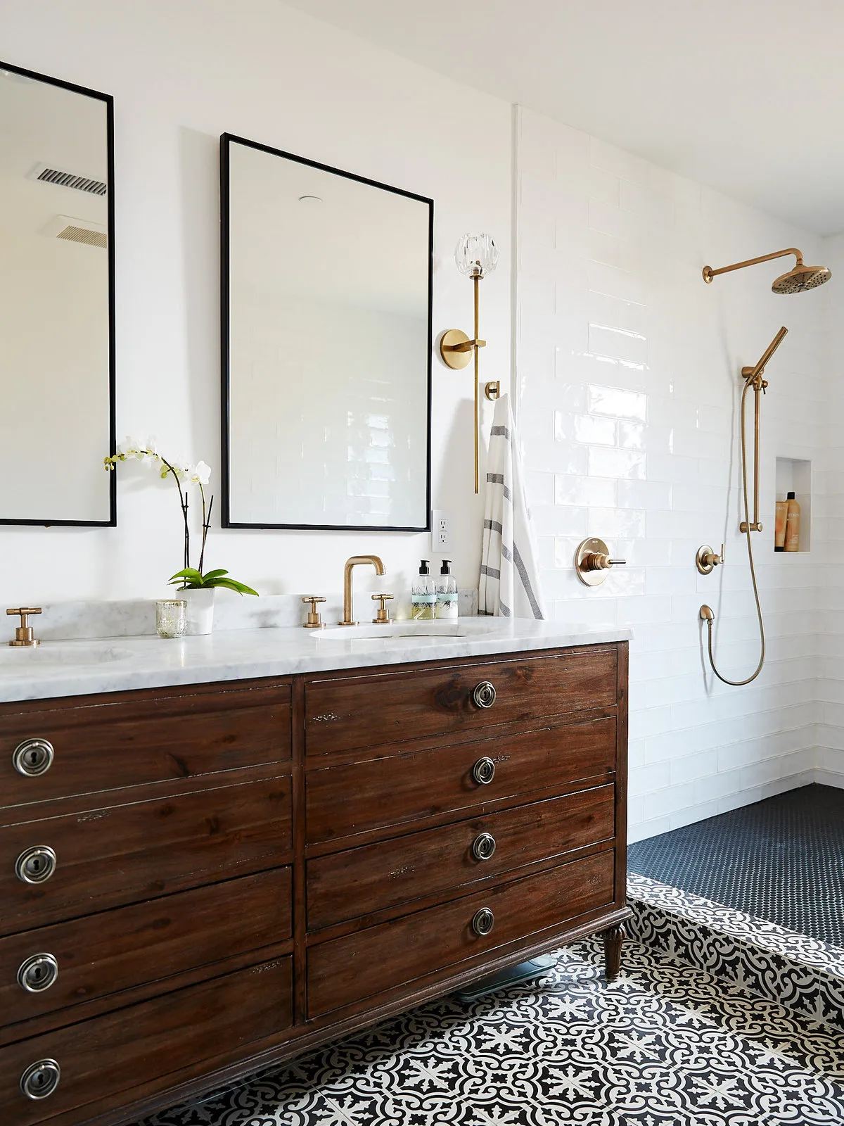 A broad timber vanity sits below simple dark-edged mirrors beside a pale shower wall.