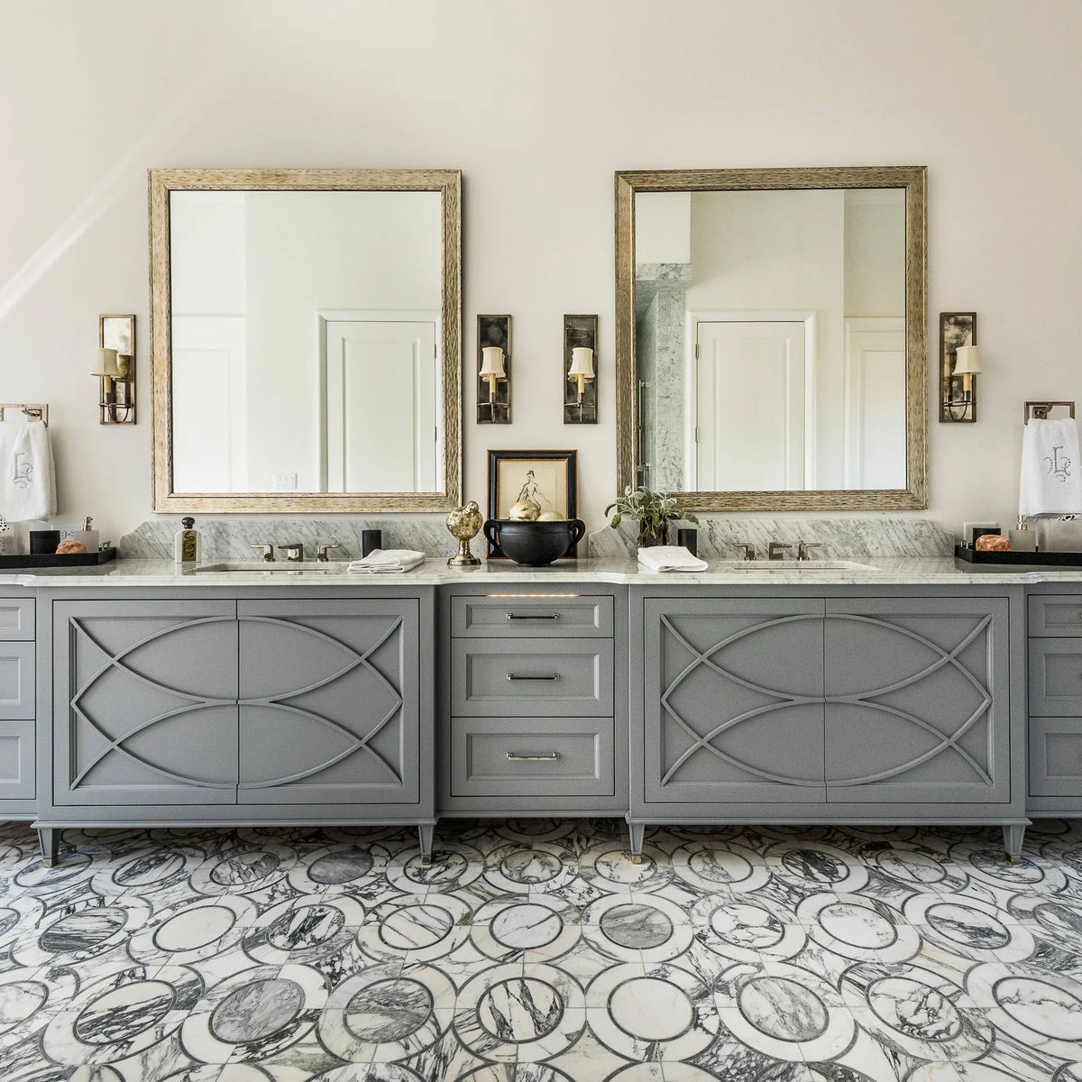 Short rectangular metal holders carry white towels at the outer ends of a gray double vanity with framed mirrors and a patterned floor.