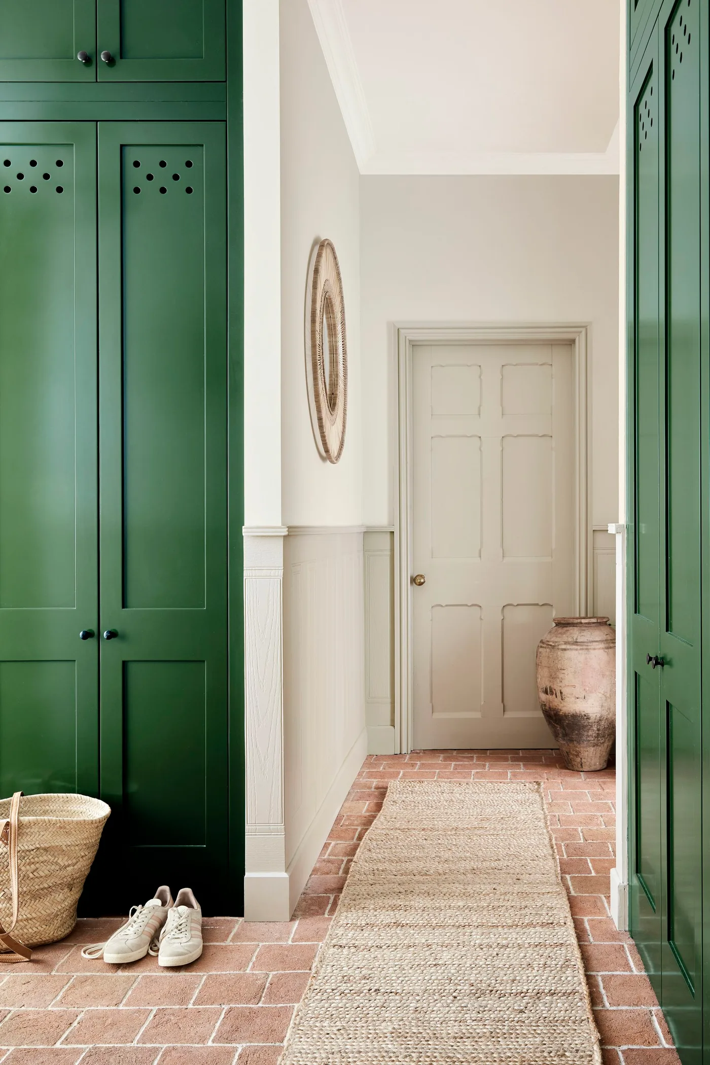 Entryway passage between tall green cupboards with a reddish brick-patterned floor and pale runner.