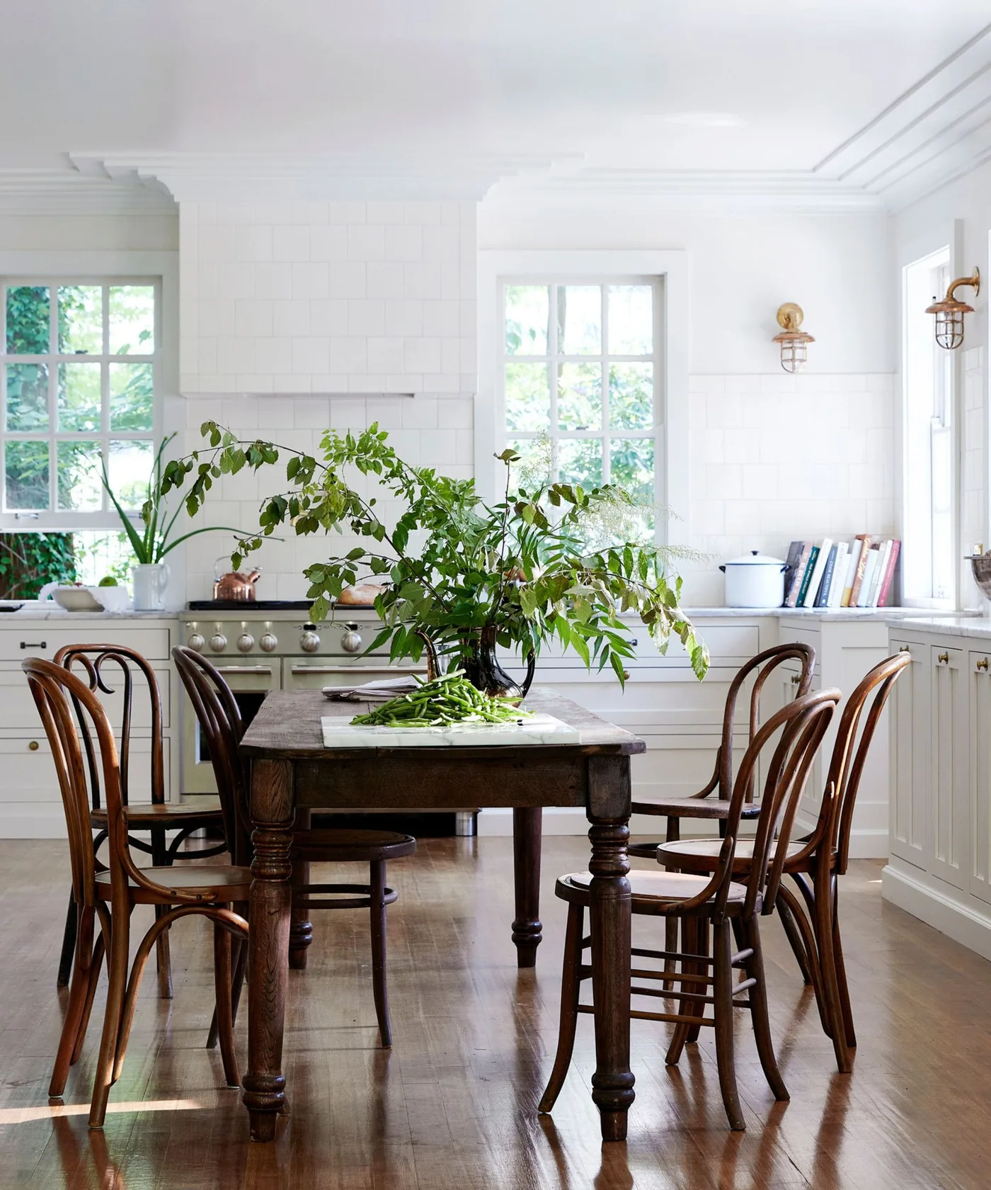 White kitchen with dark wooden turned-leg table, bentwood chairs and branches in a central vase.