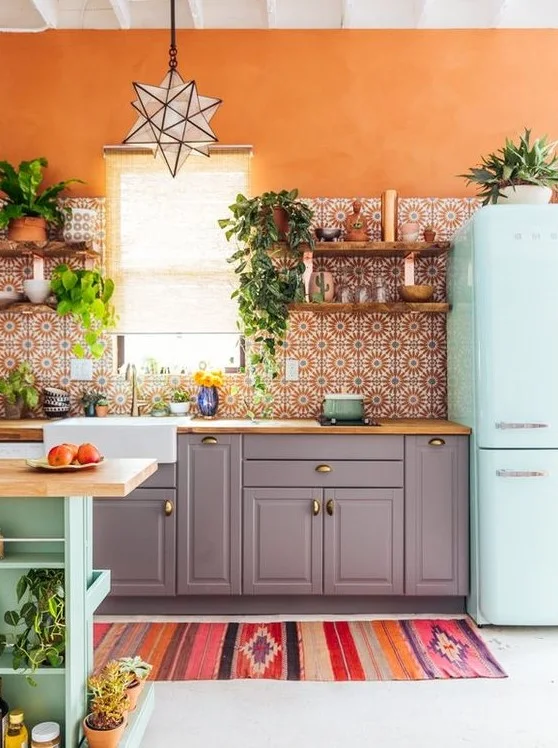 Orange walls surround patterned kitchen tiles, gray lower cabinets, a pale mint refrigerator, plants and a star-shaped pendant above a sink window