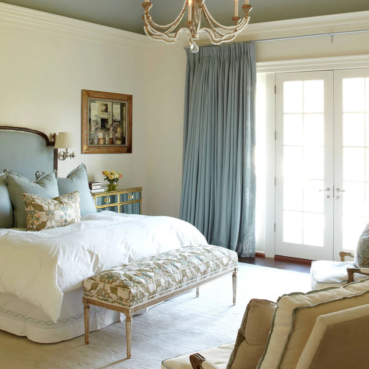 Cream bedroom walls below a muted green ceiling with pale blue curtains and an upholstered bed.