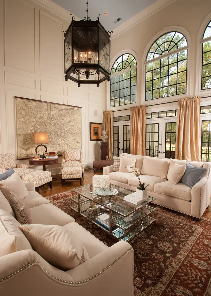 Beige sofas sit around a dark glass-topped table below a tall arched window