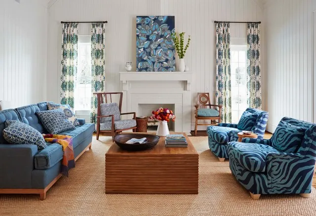 Blue patterned chairs and a sofa sit around a warm timber table beneath pale walls.