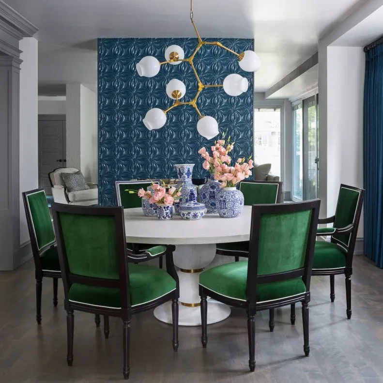 White globe chandelier on branching gold-toned arms above a round pale table and green chairs, against a blue patterned feature wall.