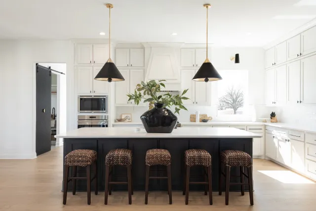 A black island anchors a kitchen with white perimeter cabinets and woven stools.
