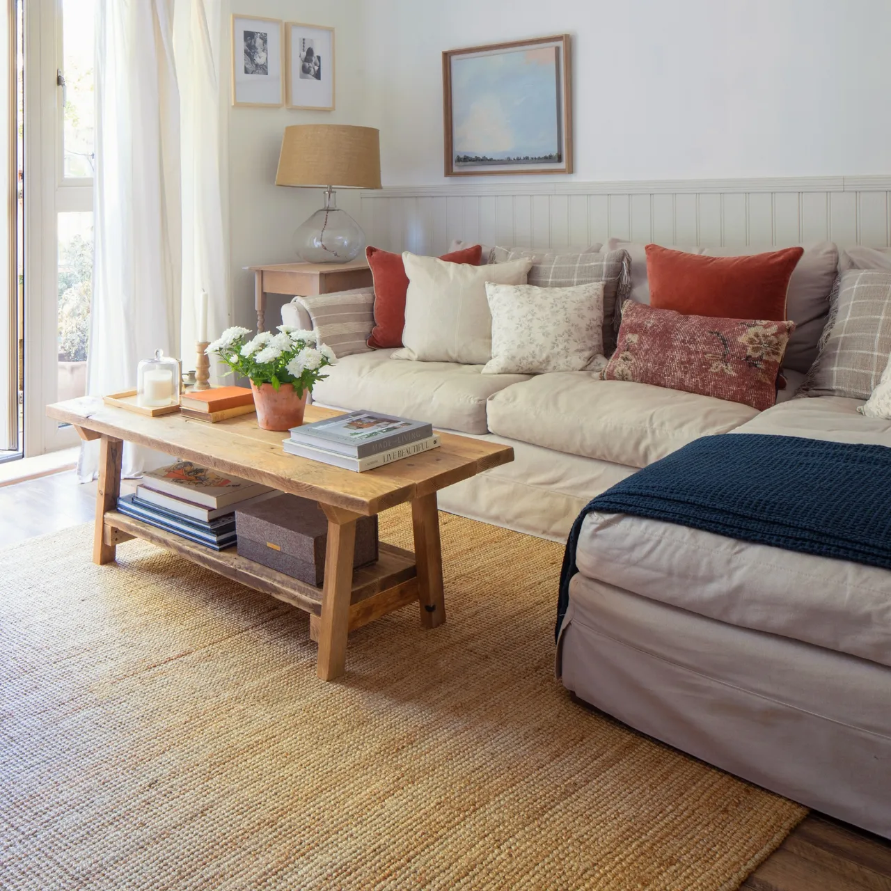 A pale corner sofa surrounds a wooden coffee table beside a bright window