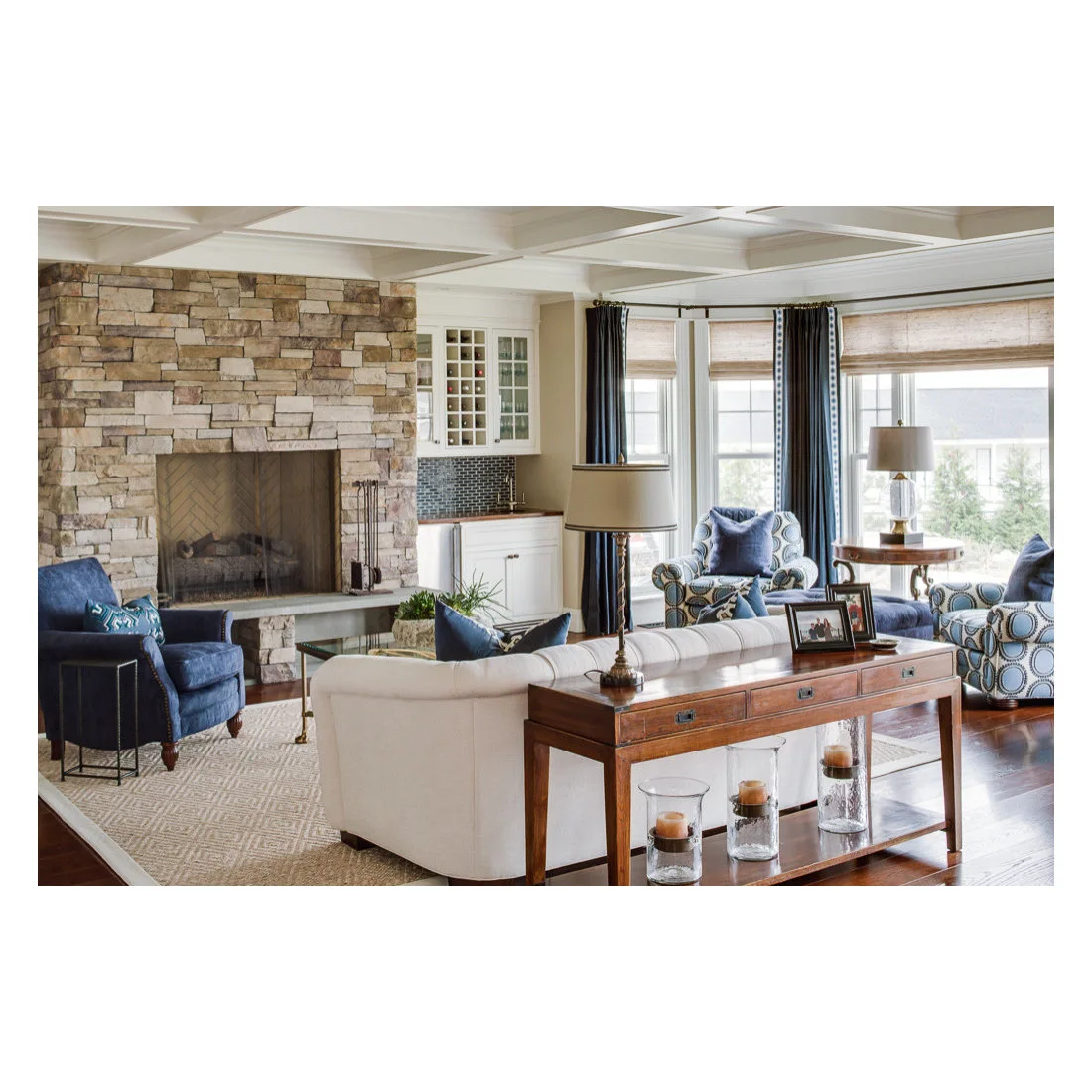 A timber console with drawers, a shaded lamp and framed photographs stands behind a pale sofa.