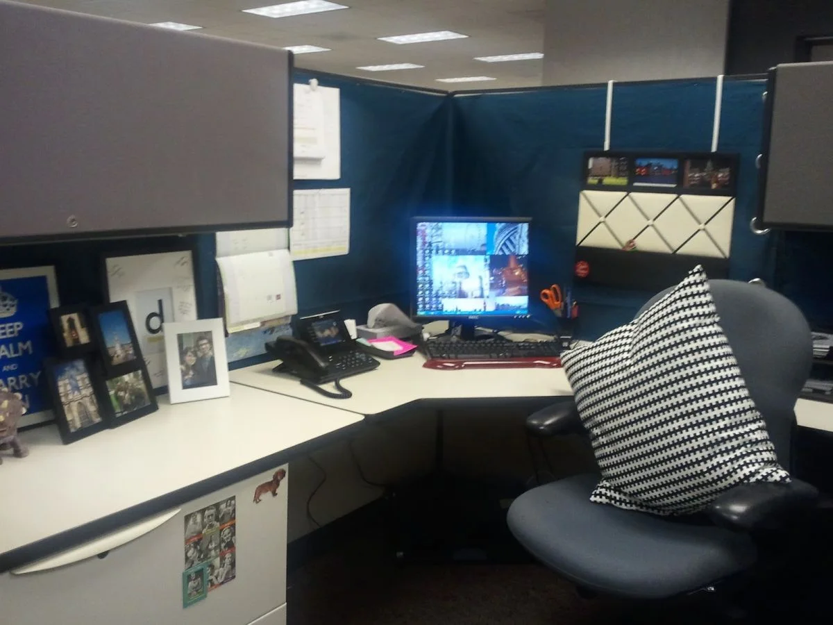 Deep blue fabric on cubicle partitions behind a monitor, personal photographs and a black and white patterned chair cushion.