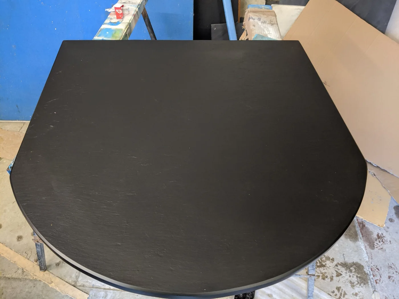 A D-shaped riven slate hearth with a straight back and rounded front sits on workshop stands.