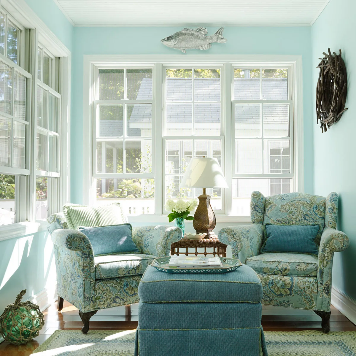 Two blue-green patterned armchairs share an ottoman and side table in a small room with pale aqua walls.