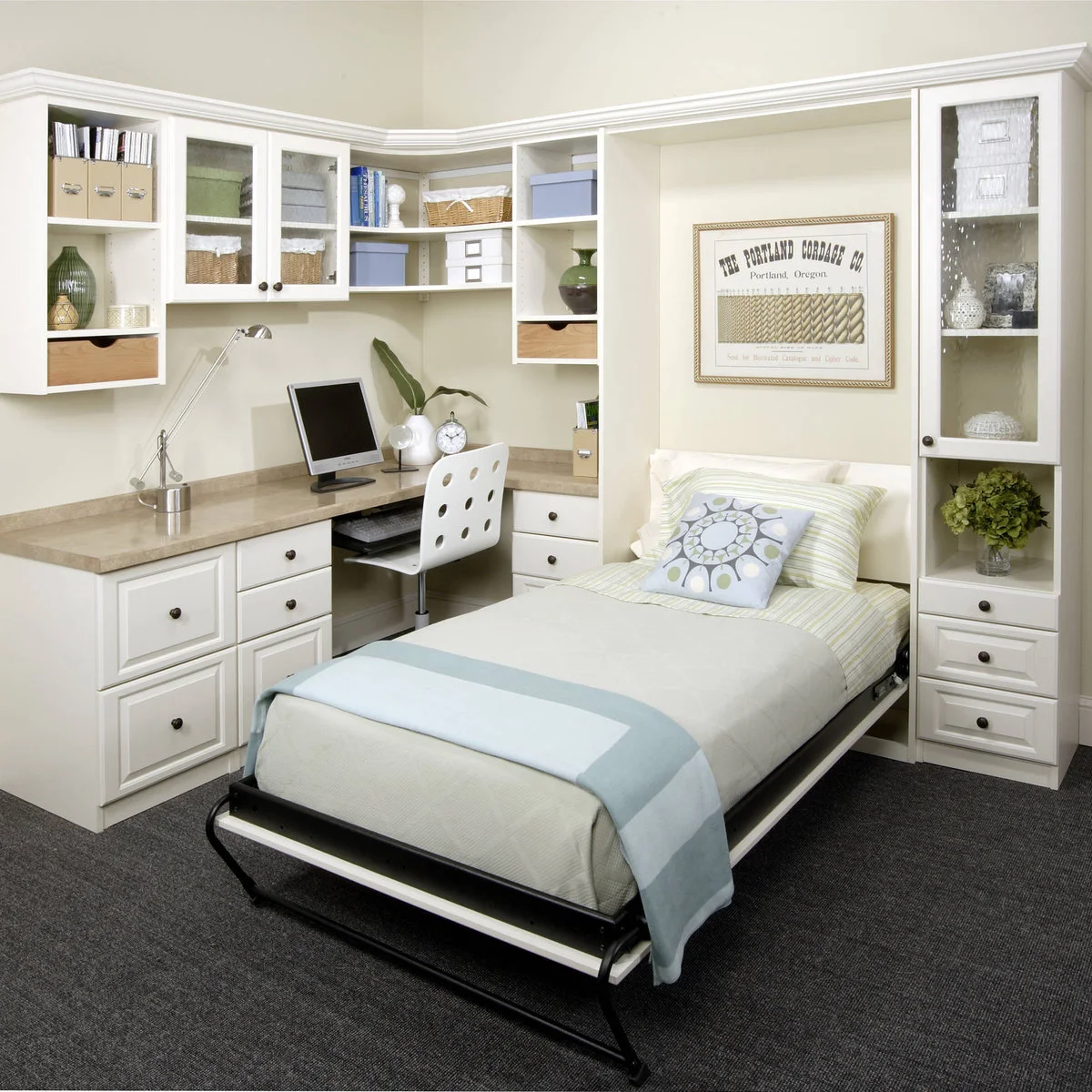 Small single fold-down bed open beside a fitted desk and white storage cupboards