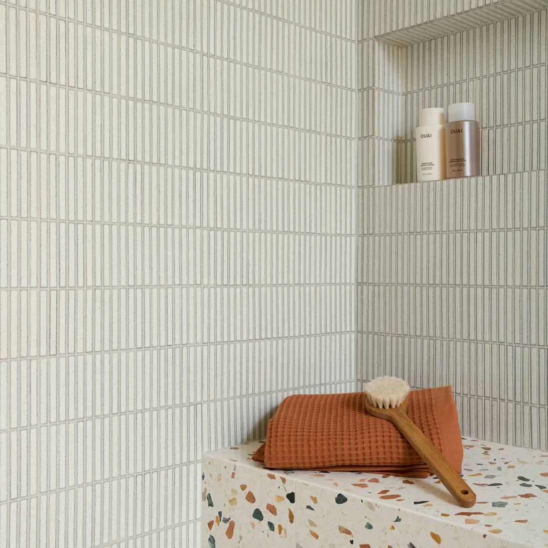 Large colored terrazzo chips cover a shower bench beneath fine vertical wall tiles and a recessed niche.
