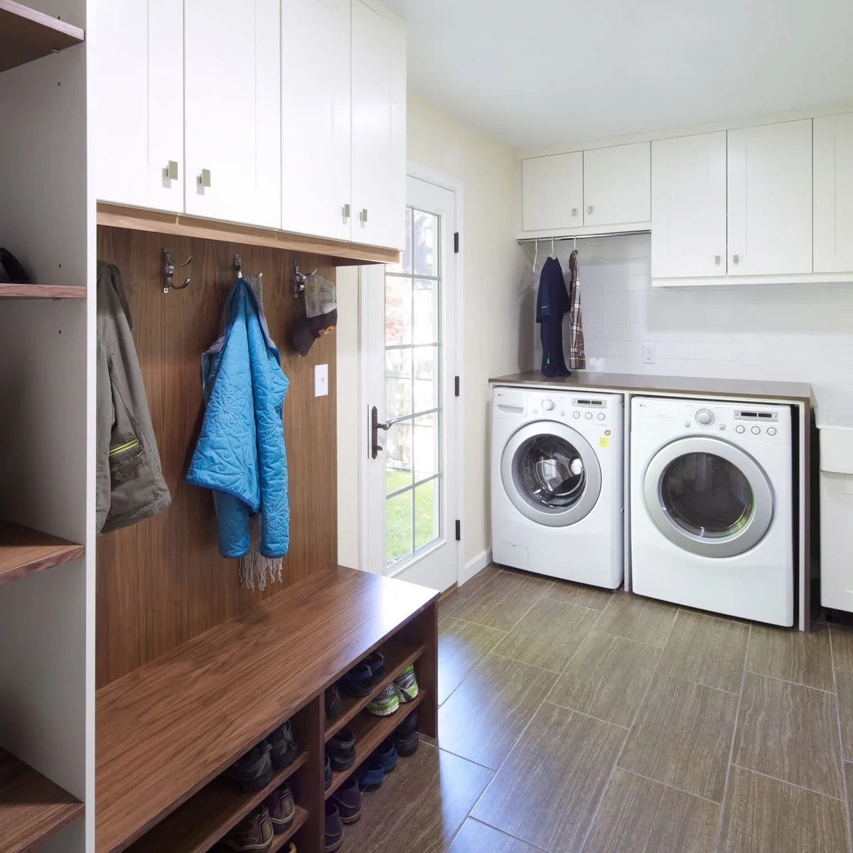 Combined laundry and entrance room with a wood-toned shoe bench, coat hooks, glass door and white machines under a counter