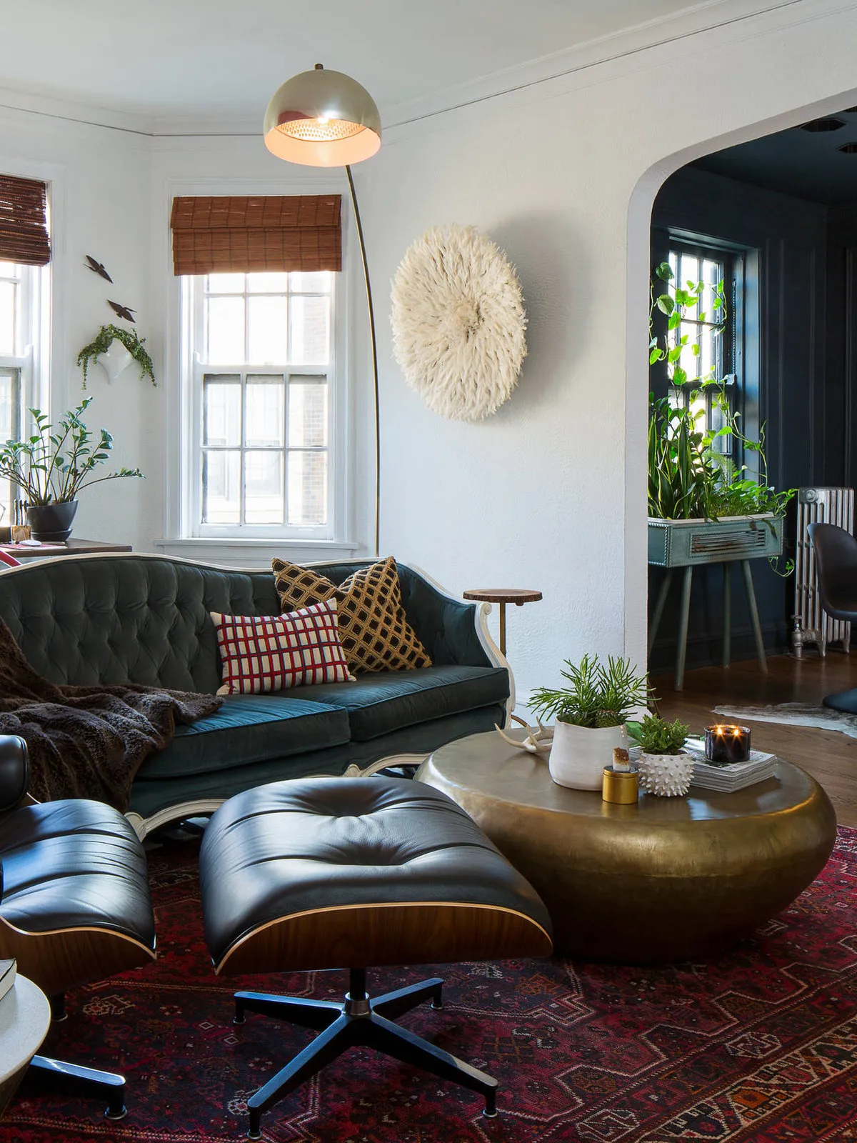A dark lounge chair and footstool share a room with a green sofa and patterned cushions.