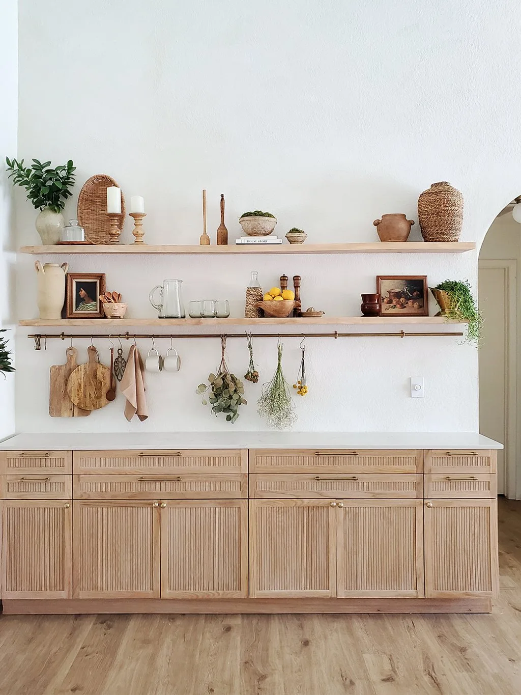 Two pale wood shelves above a fluted dining serving cabinet with a rail for cups and boards