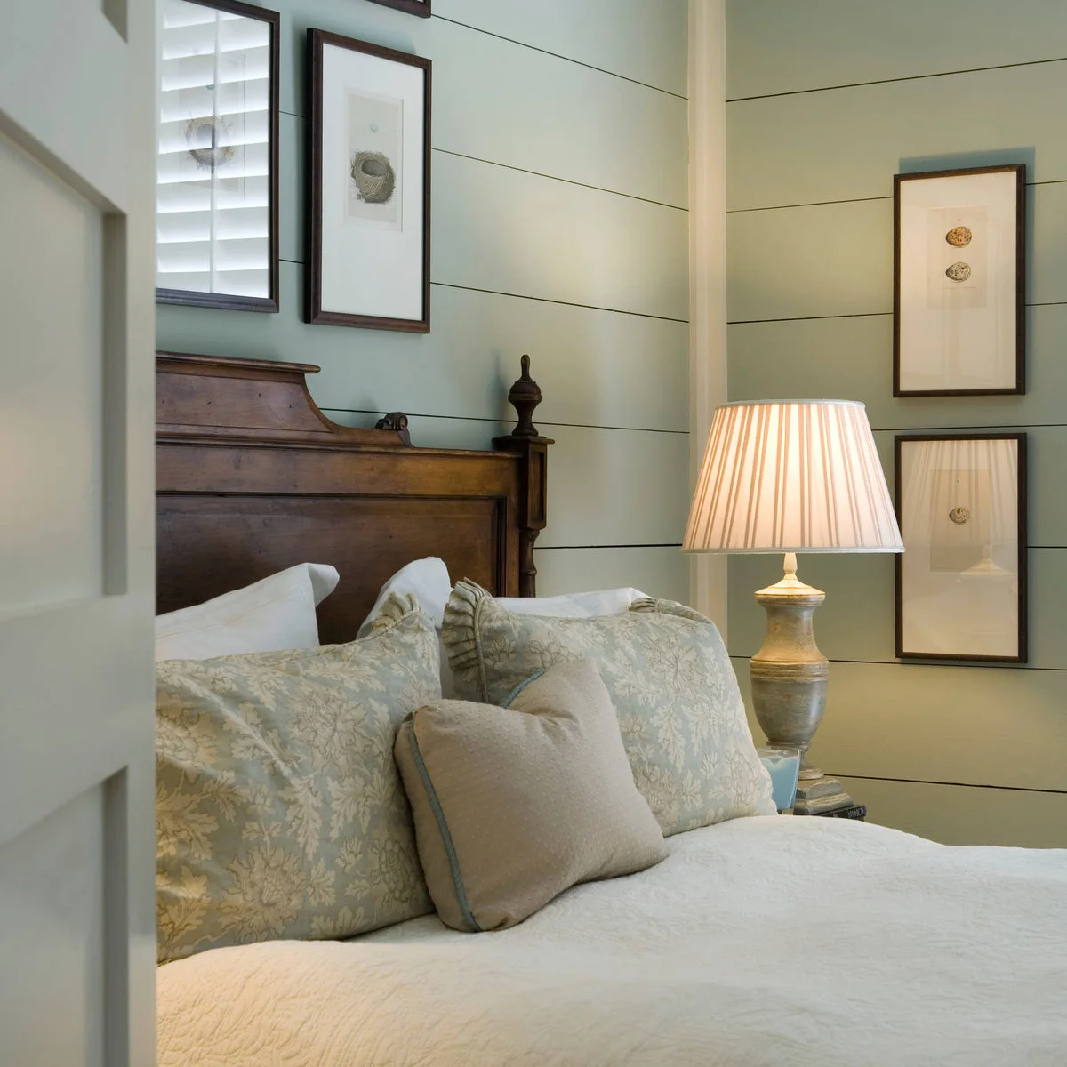 Bedroom with a pale sage horizontal-board wall, wood headboard, mint floral pillows and cream quilt