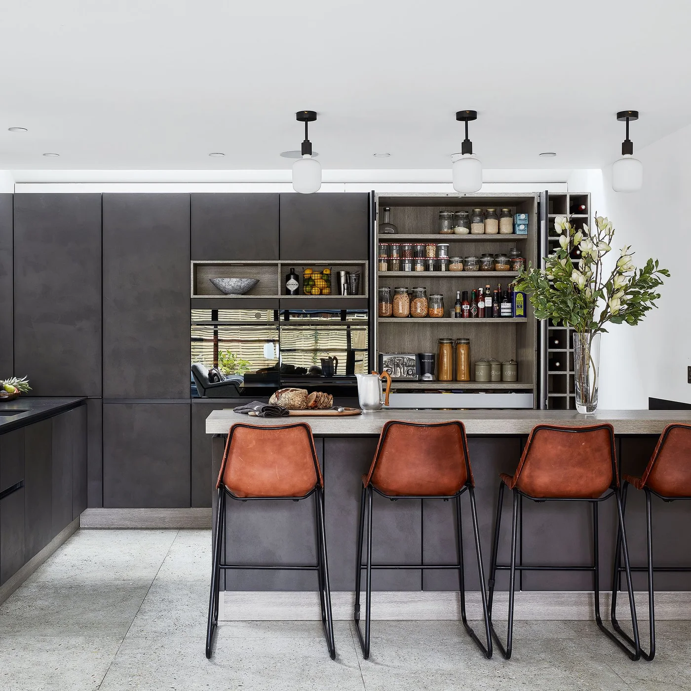 Dark flat-front kitchen cabinets include an open pantry beside orange-brown stools and a gray island