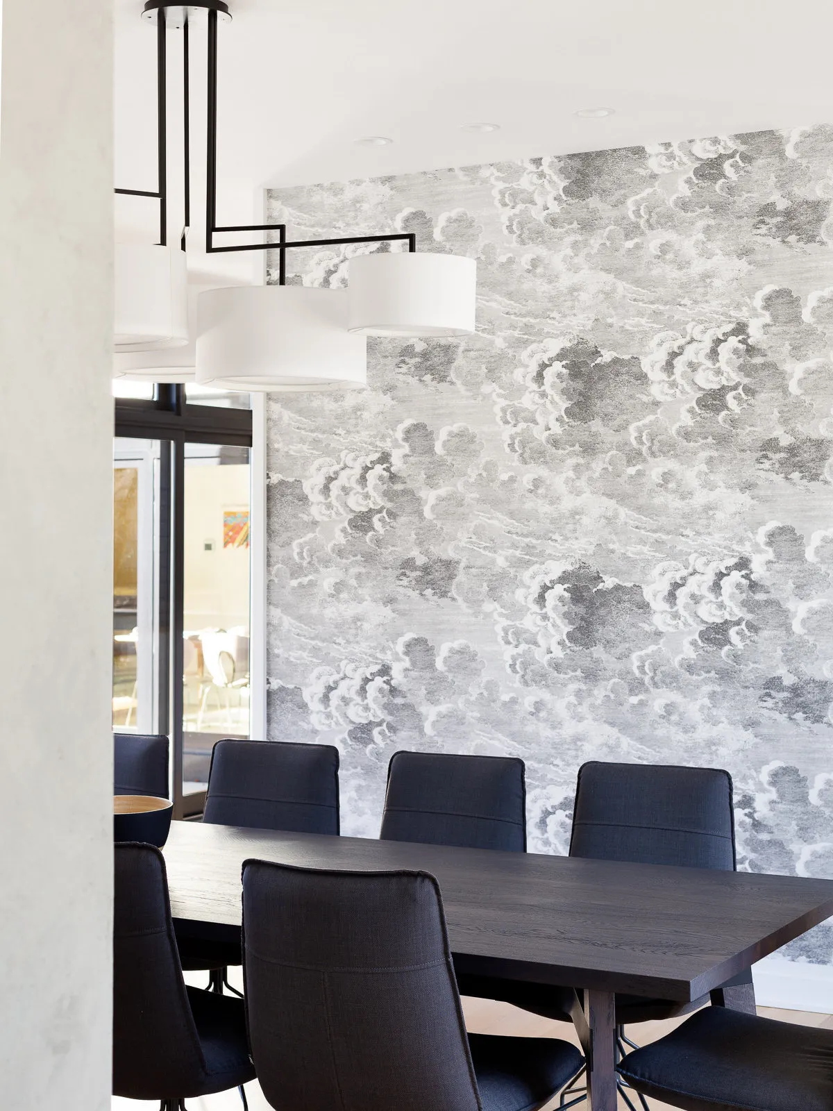 A pale botanical wall sits behind dark dining chairs and a black table.
