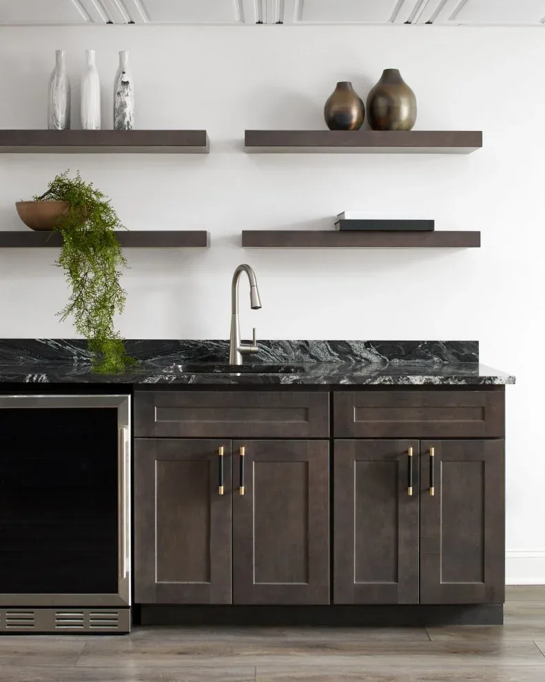 Four short dark floating shelves with vases, a trailing plant and a book above a dark drinks counter