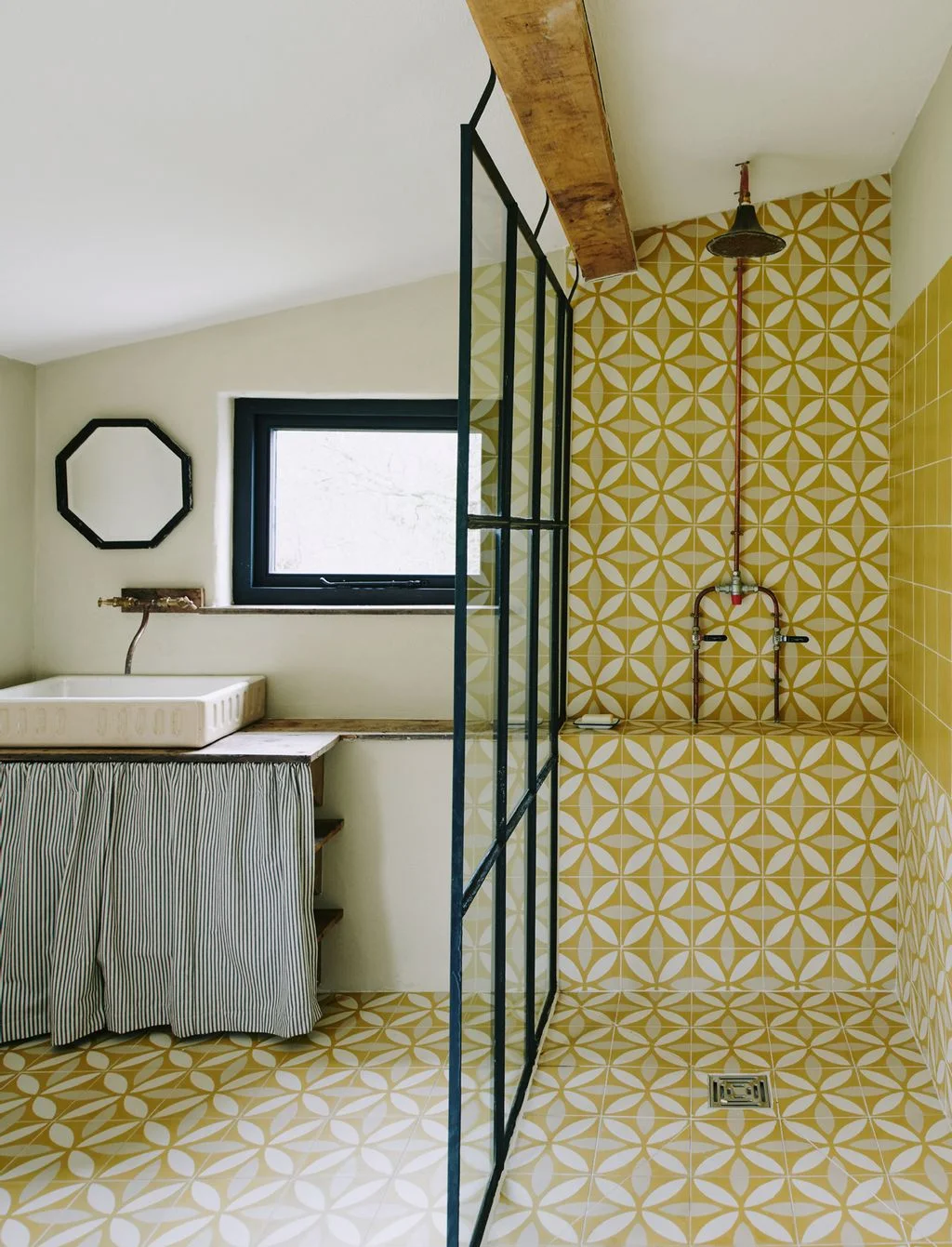 A black-framed fixed screen borders a yellow patterned walk-in shower beside a skirted sink under a sloping ceiling.