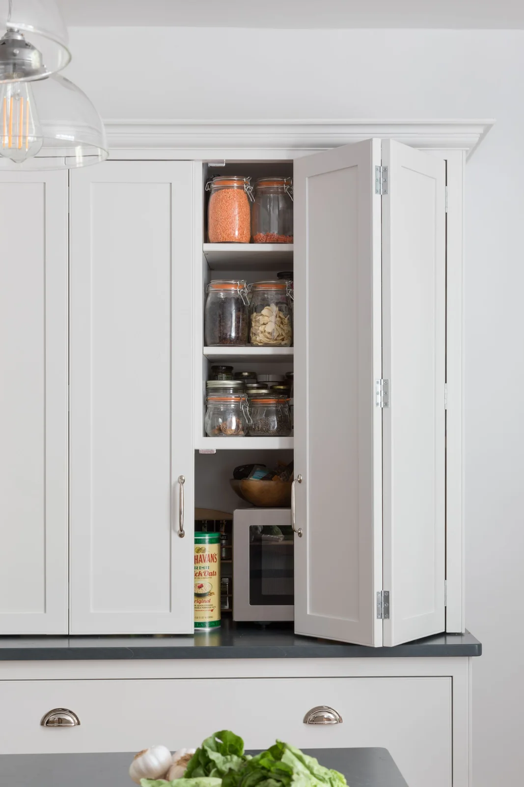 White countertop cupboard with clear jars on shelves behind folding doors