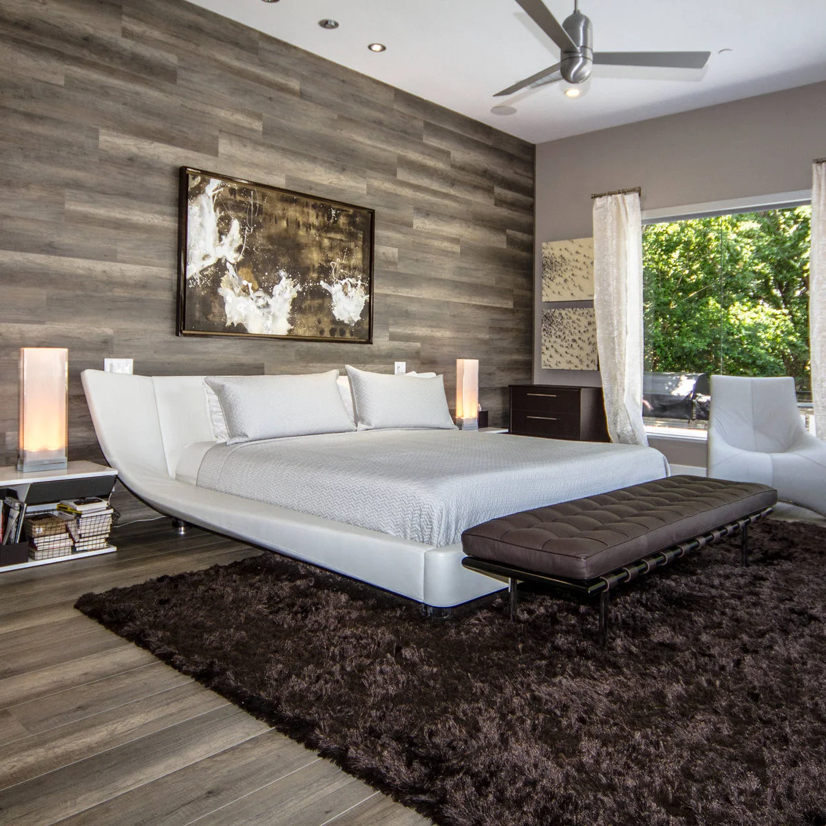 Gold and white abstract picture above a curved white bed against a wall of horizontal gray-brown boards.