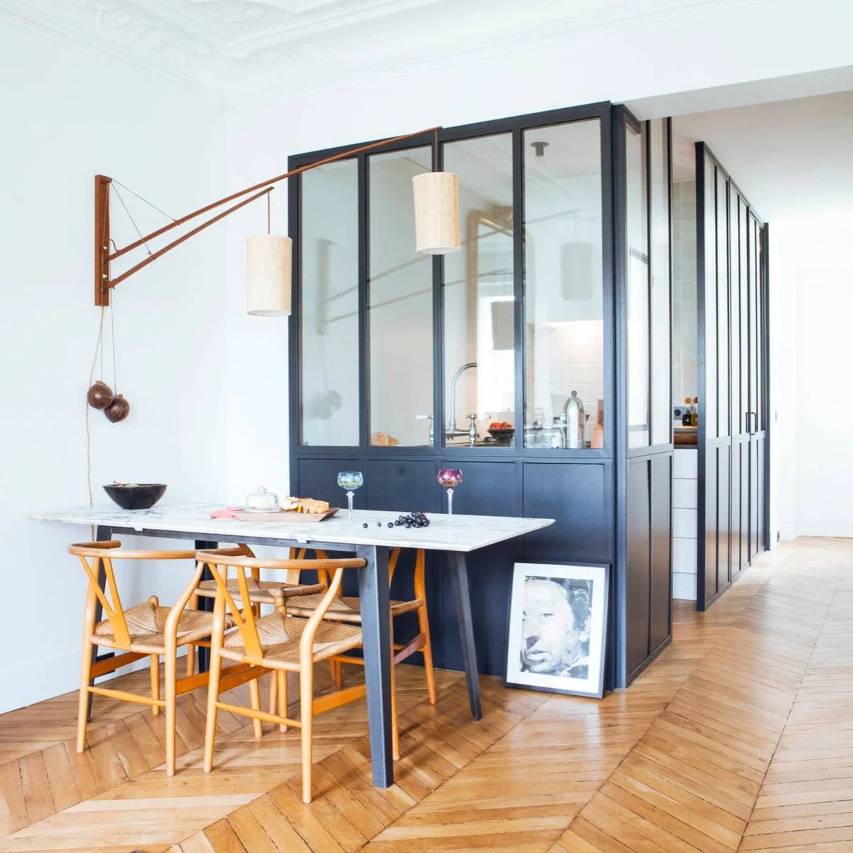 A dark-framed glazed kitchen enclosure turns a corner beside a dining table with wood chairs.