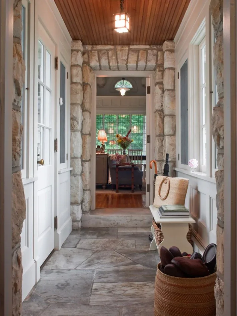 A small white freestanding bench stands beneath a window in a stone-walled passage with a wood ceiling and baskets.