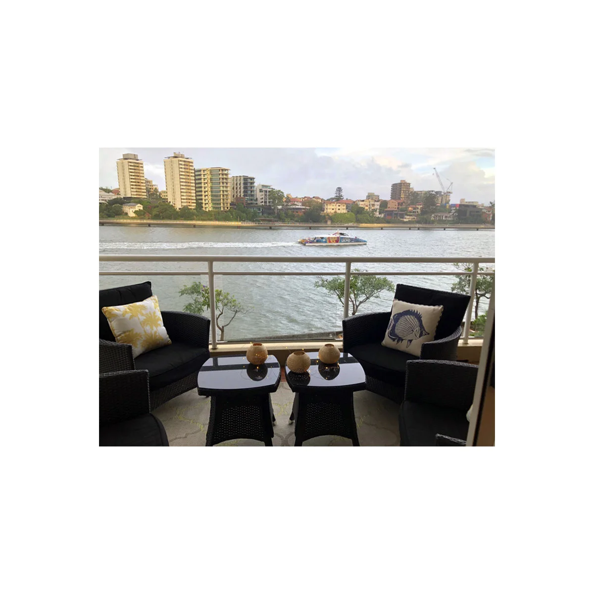 Riverfront apartment balcony with dark woven-looking chairs and two small square tables