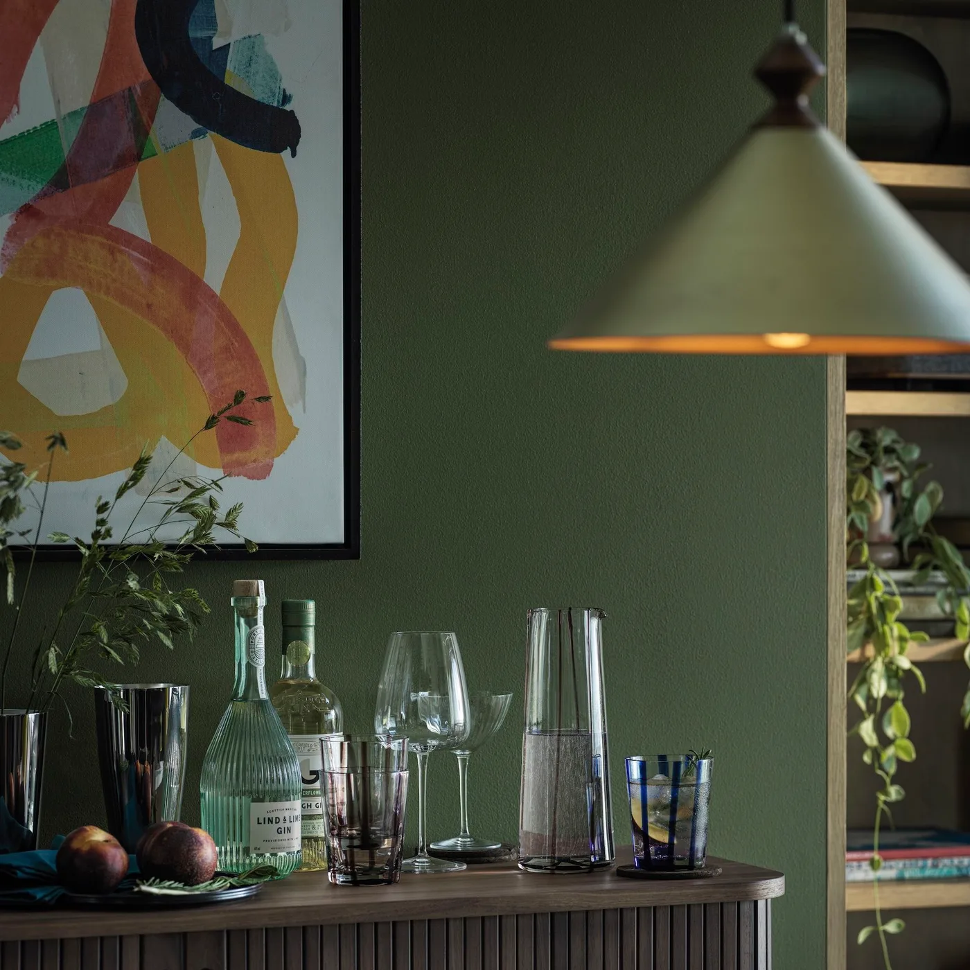 Green pendant above a dark fluted sideboard holding bottles and glassware against a green wall