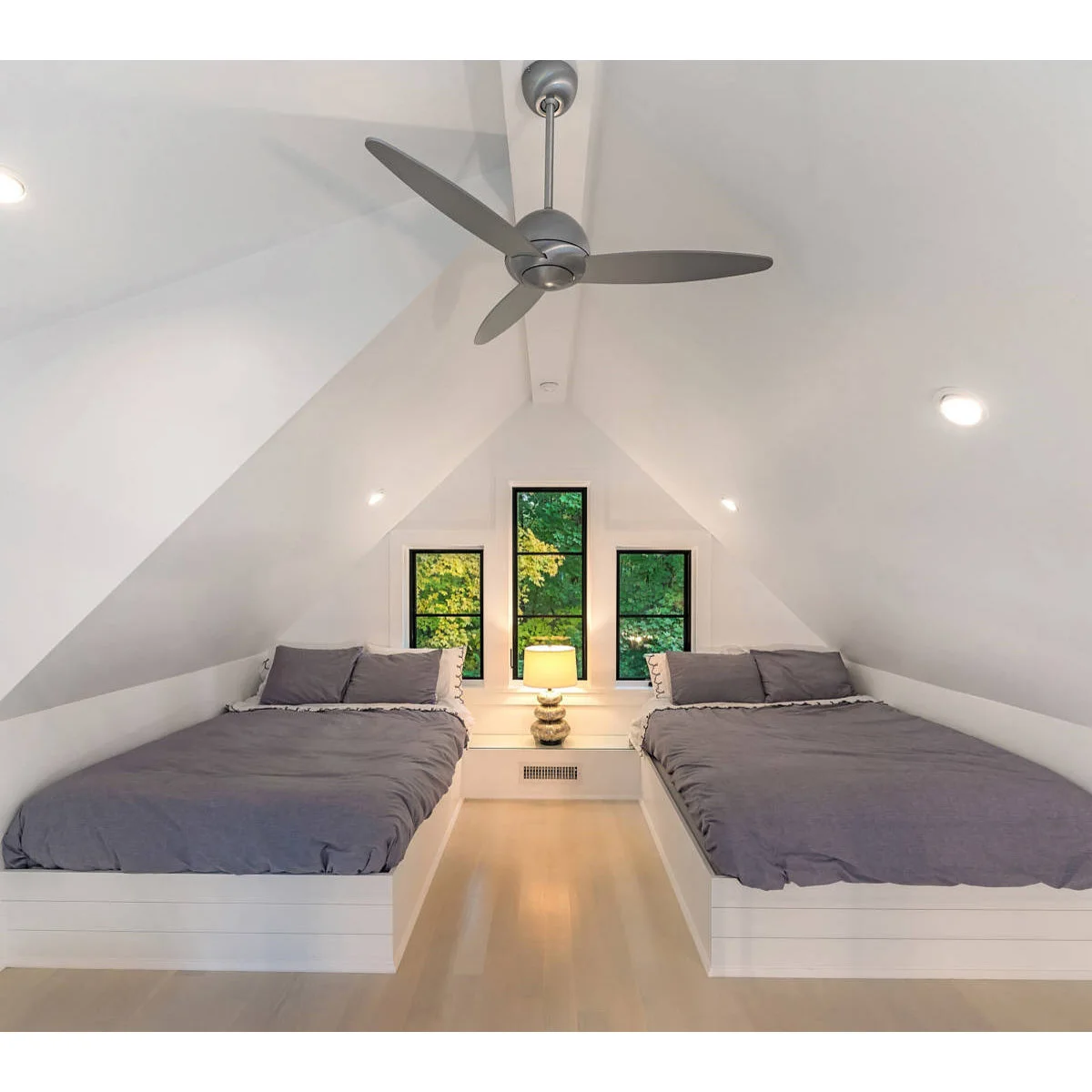Two gray-covered beds positioned along the low sides of a white attic room with a clear central aisle.