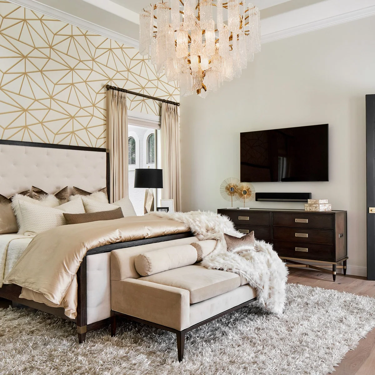 Gold and white angular wallpaper around a bedroom window behind a pale upholstered bed with a dark frame.