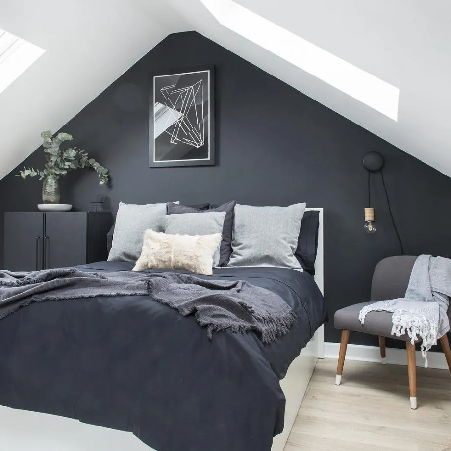 A dark bed sits against a charcoal gable wall beneath bright roof windows