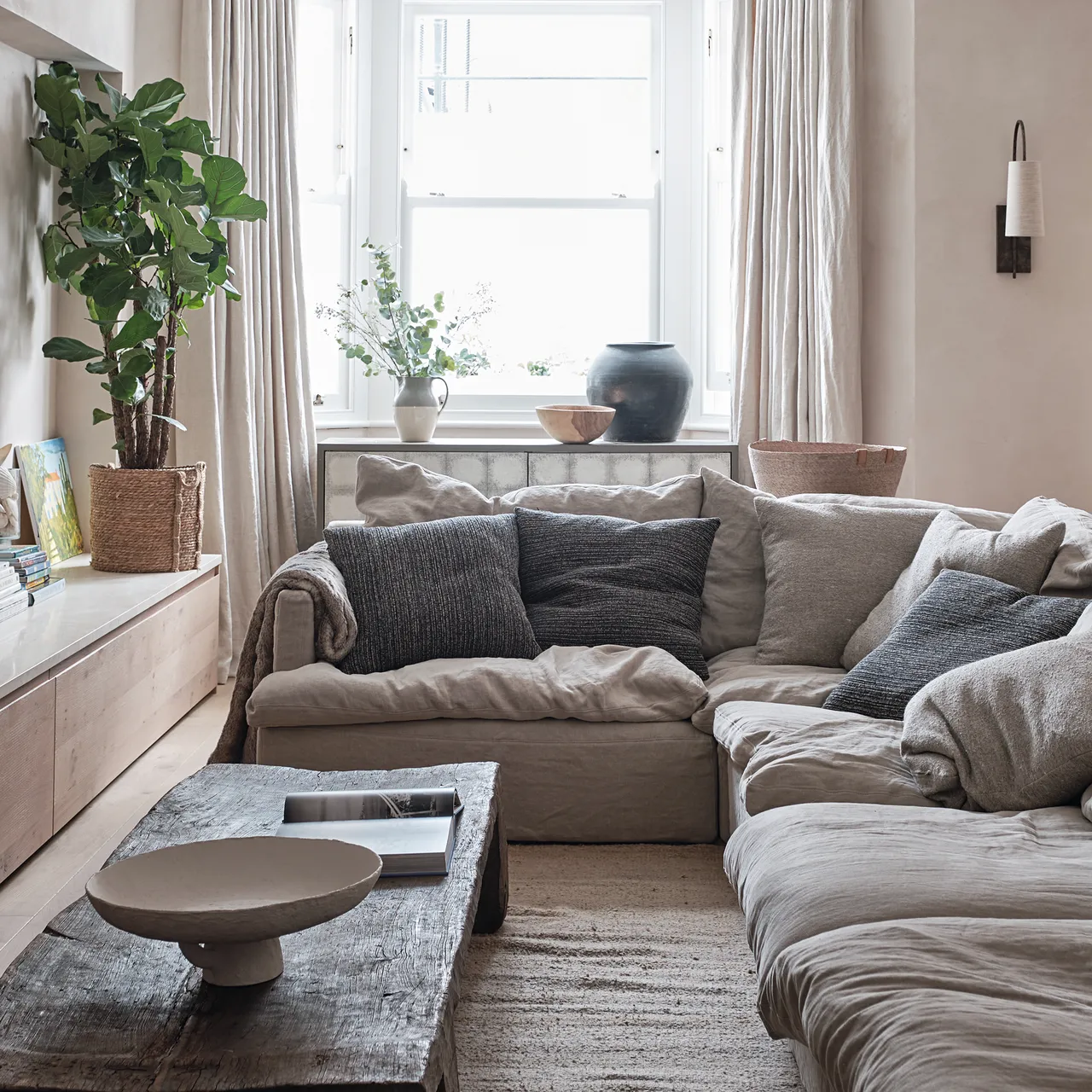 Pale greige corner sofa with dark cushions beside a textured rug and wood table