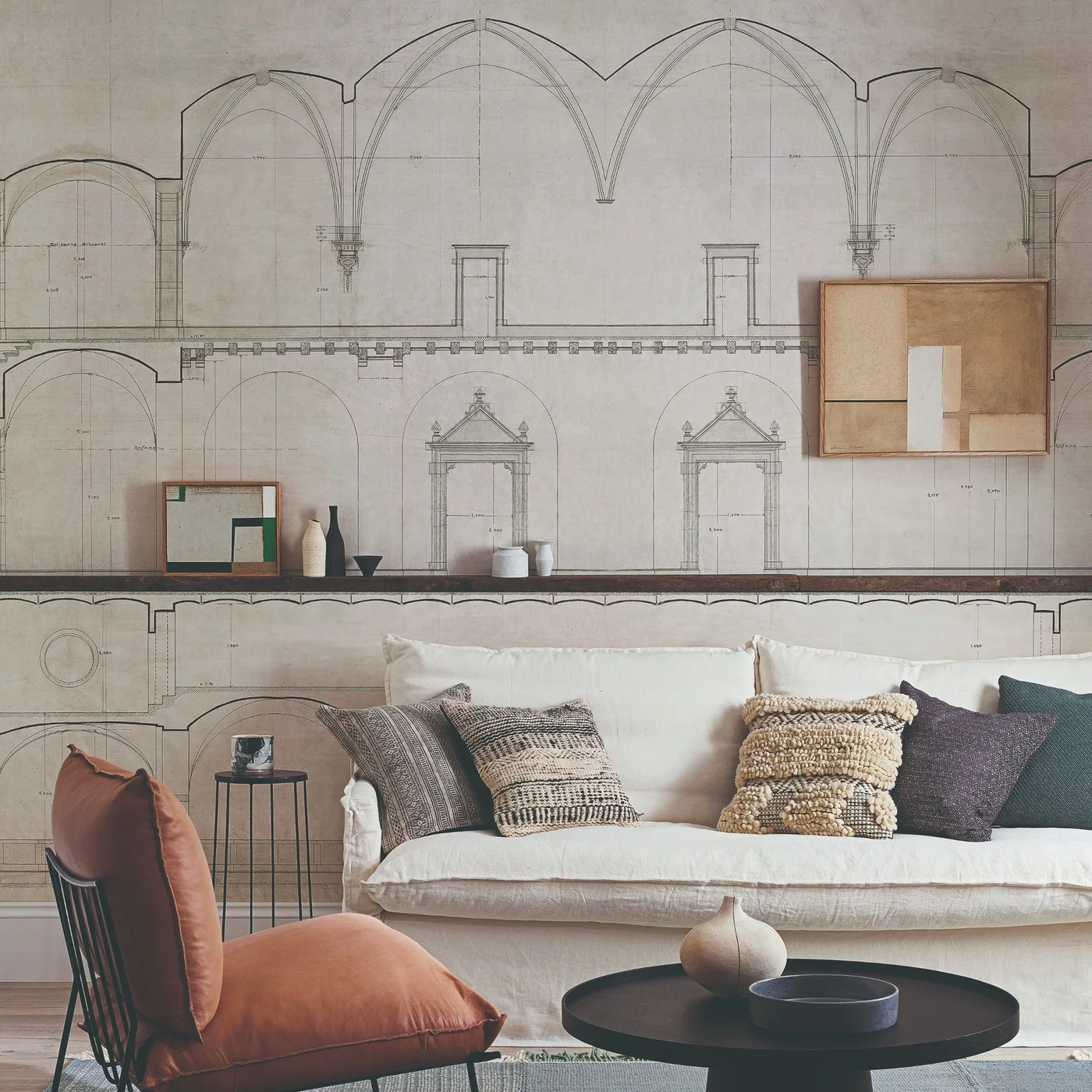 A pale sofa and dark round table sit before an architectural line-drawing wall mural and narrow display ledge.