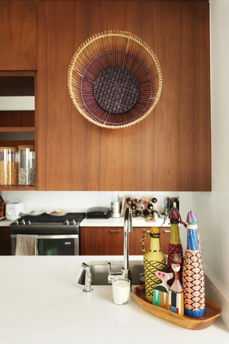 Kitchen with warm wood upper cabinets, a large woven circular wall piece and colorful bottles beside the sink.