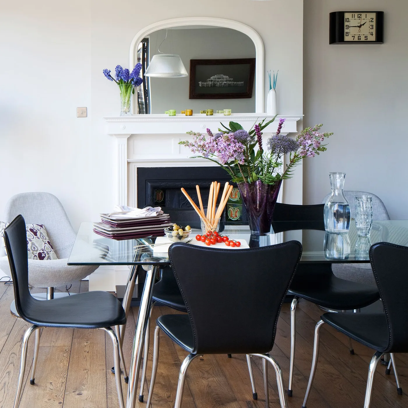 White arched mirror above a white mantel behind a glass dining table with black chairs