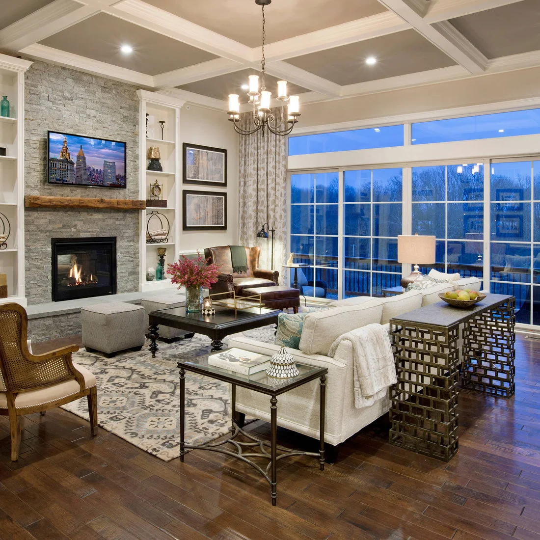 A dark console with a geometric lattice frame stands behind a pale sofa beside large windows.