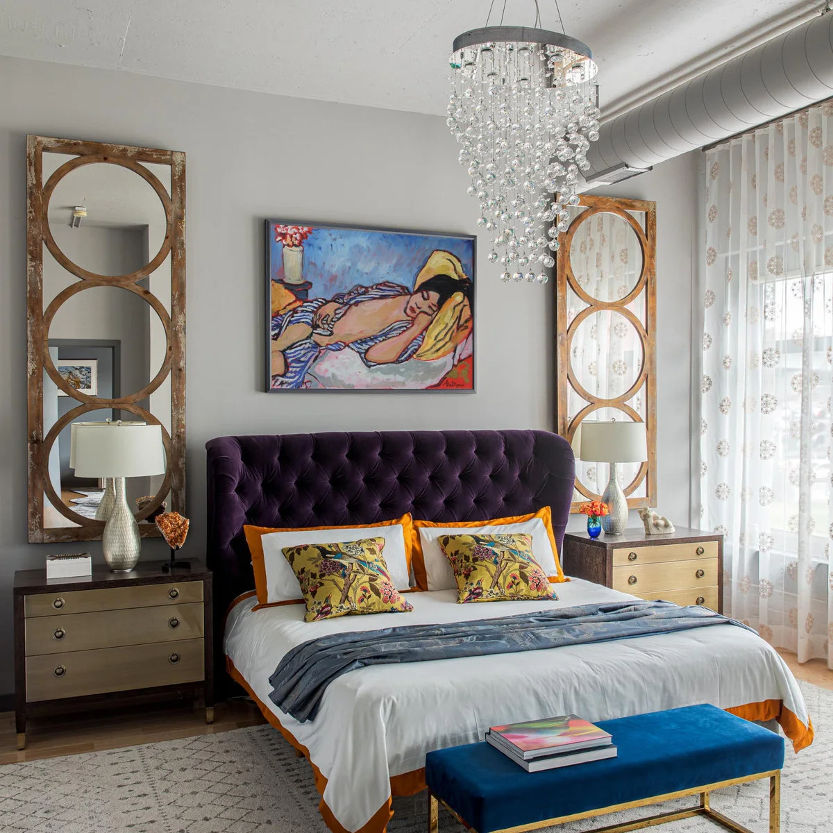 Colorful reclining-figure painting above a purple tufted headboard between tall decorative mirrors with a blue bench.