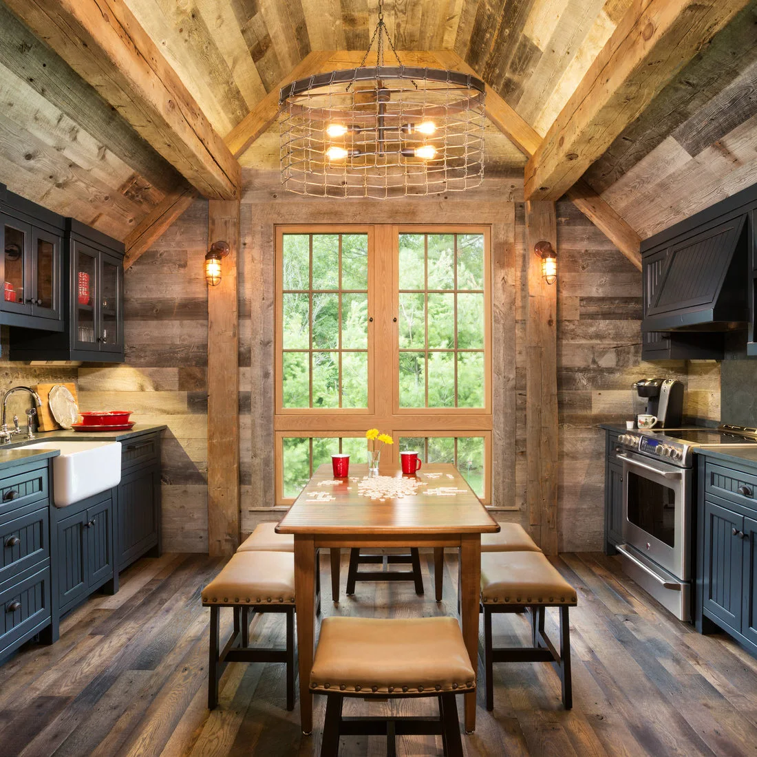 A small dining table with padded benches between dark cabinets beneath a pitched timber roof
