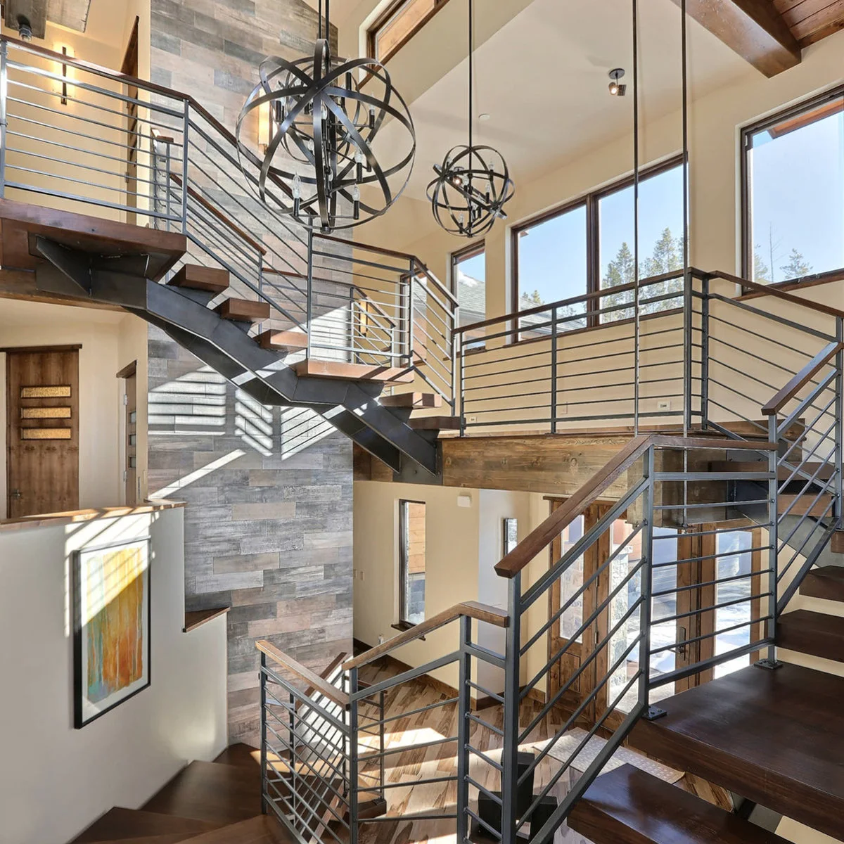 A tall narrow stone-clad strip rises through an open staircase beside large windows.
