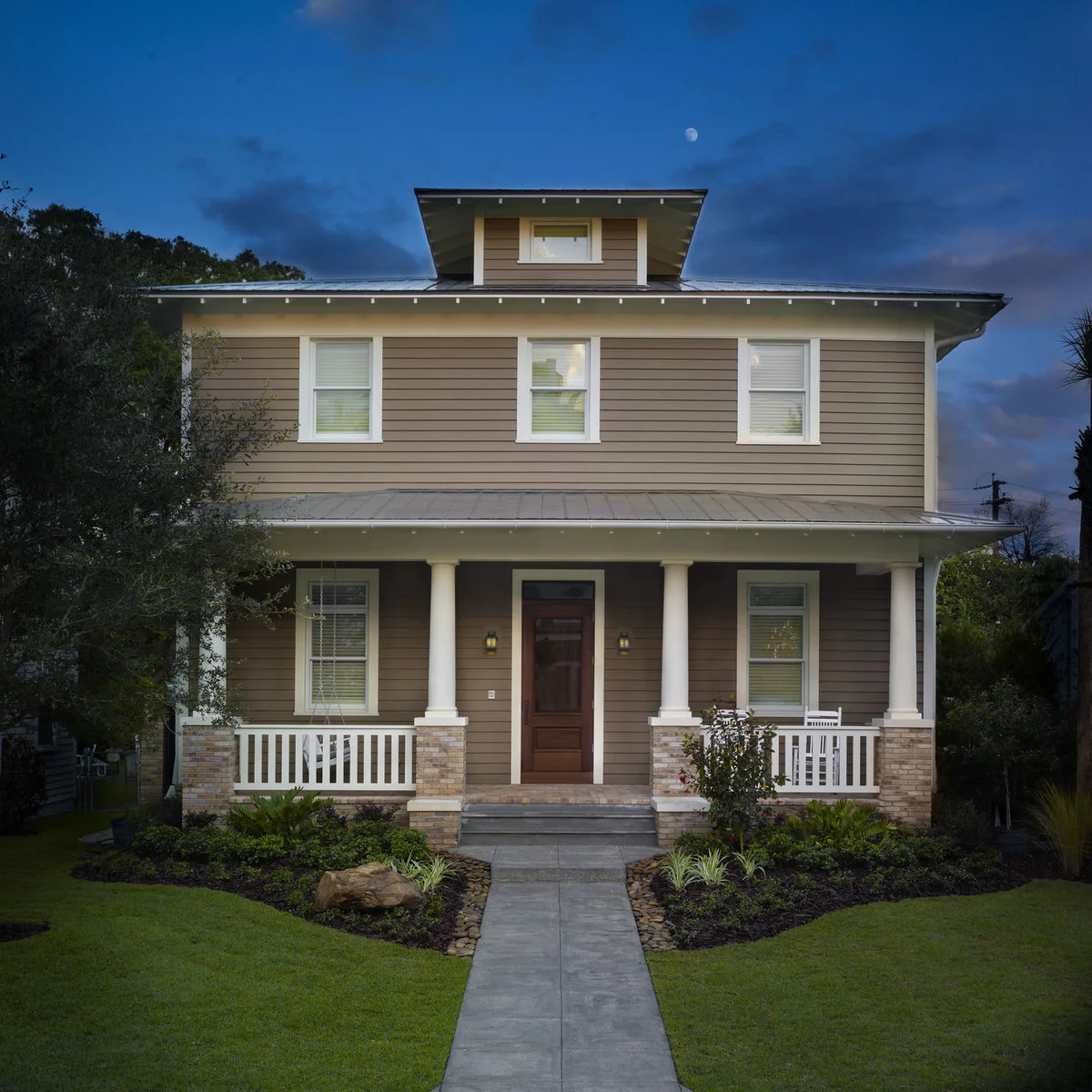 A tan house with a front porch, small rounded shrubs in dark mulch and pale stones along the approach.