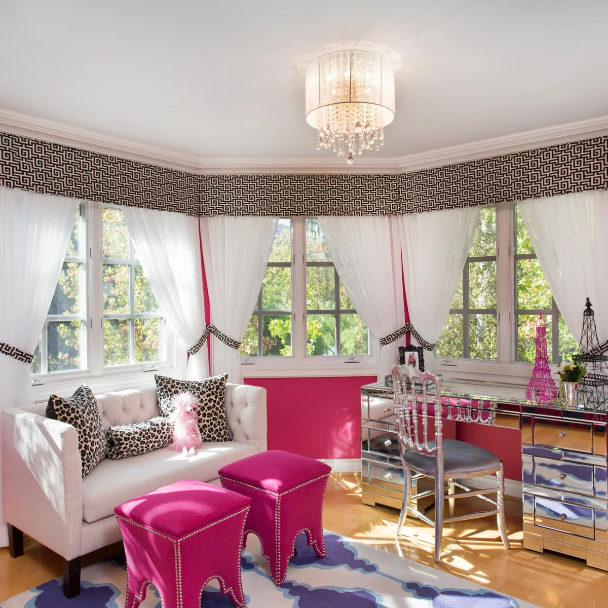 White settee and mirrored desk with hot pink stools beneath patterned window trim
