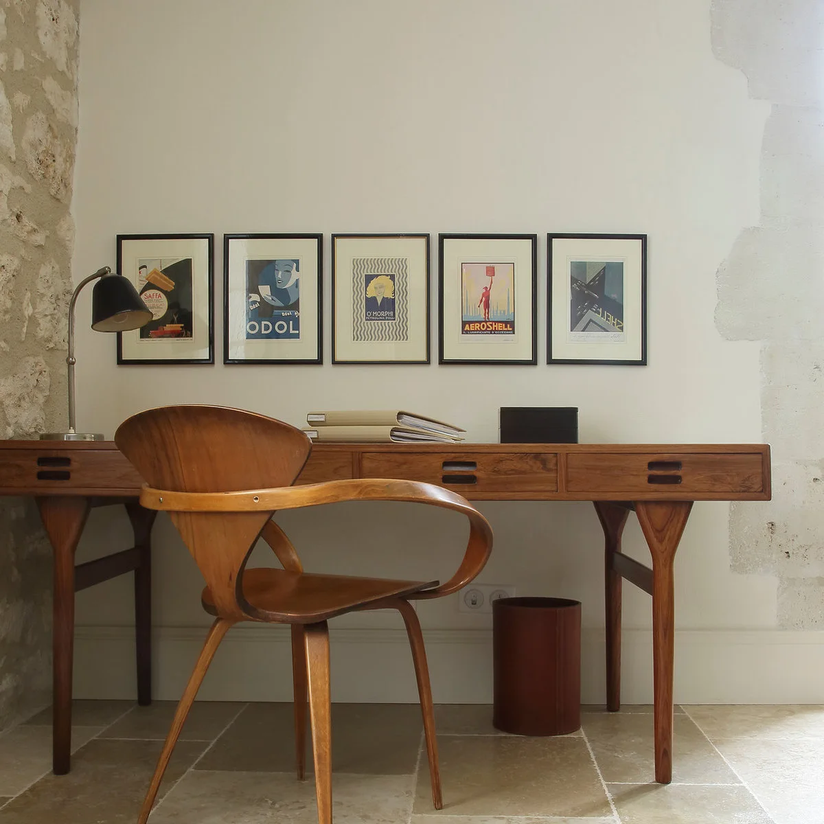 Wood writing desk with slim legs and shallow drawers beneath five framed prints