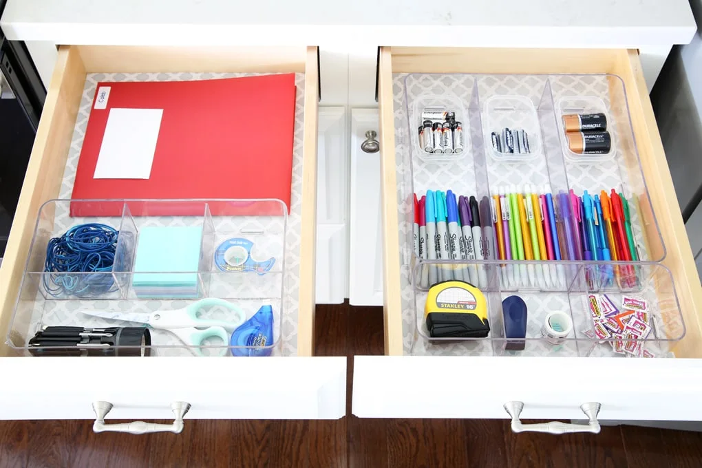 Two adjacent white drawers with clear organizers separating paperwork and scissors from pens and batteries