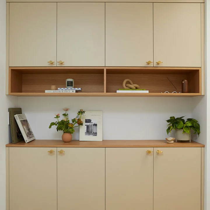 Cream wall and base cupboards contain wood-lined open niches and a wood counter with small plants and books.