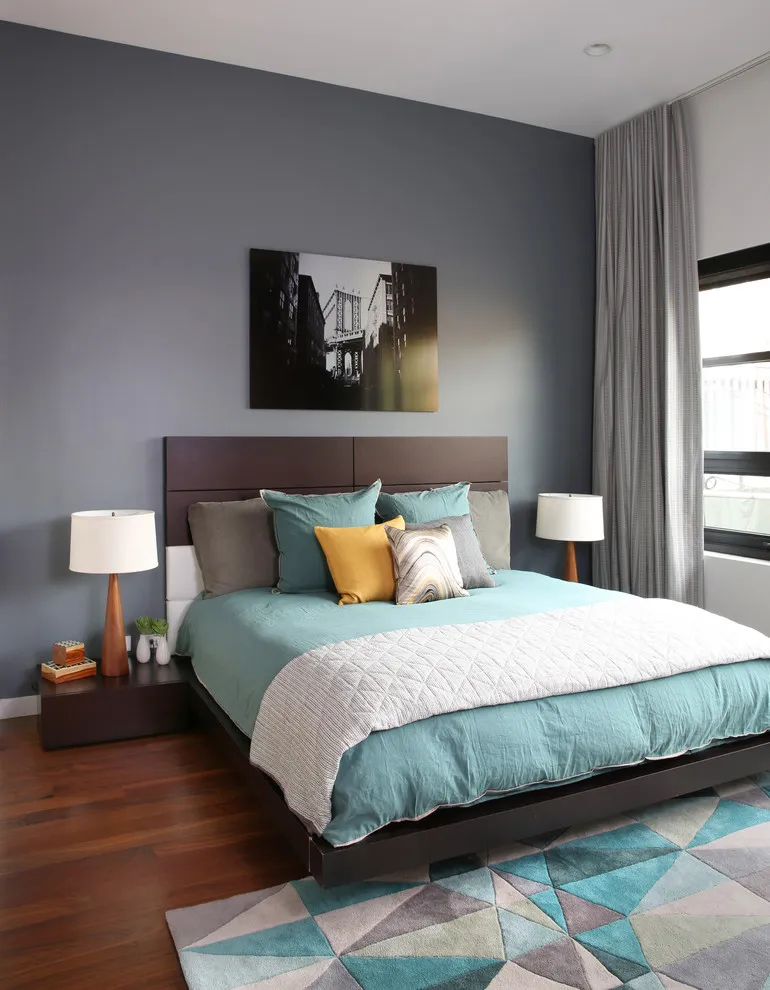 A dark gray wall frames a bed with turquoise bedding and a geometric rug